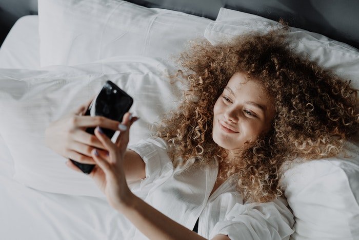 Una niña tomando un selfie acostada en la cama
