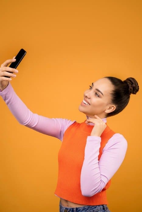 Una mujer joven posando para un selfie de alto ángulo delante de un fondo naranja