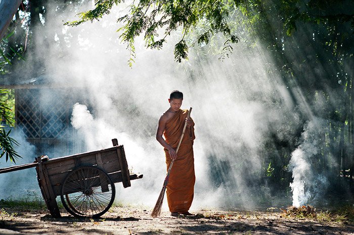 Hermoso retrato de luz de borde de un monje budista barriendo al aire libre