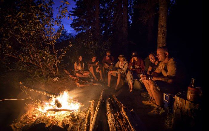 Un grupo de personas sentadas alrededor de una fogata en un bosque por la noche