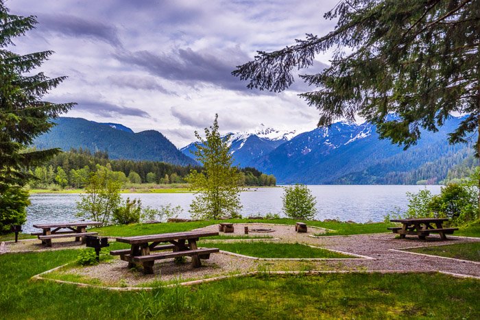Un área de picnic en un campamento con un lago y montañas al fondo.