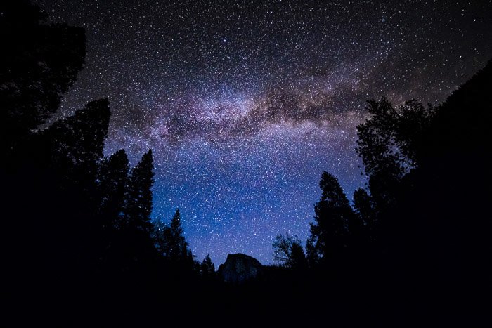Toma de astrofotografía de fotograma completo de las siluetas de los árboles en el primer plano de un impresionante cielo nocturno lleno de comienzo.  Tomada con lente rokinon de 14 mm