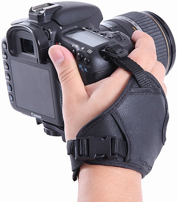 Un primer plano de una mano, sosteniendo una cámara réflex digital con una correa para la muñeca