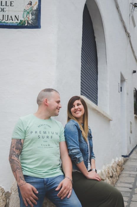 Hombre y mujer sentados en la esquina de un edificio blanco, sonriendo amorosamente