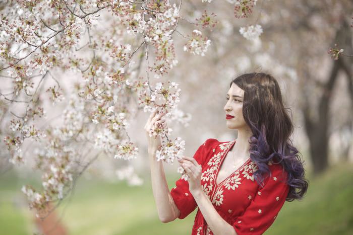 Una modelo femenina en vestido rojo sosteniendo las ramas de un árbol de cerezos en flor