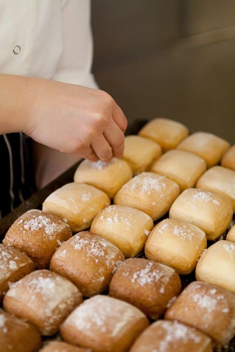 Cerca de la mano del panadero espolvorear azúcar en bollos recién horneados