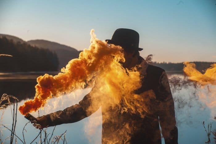 Un hombre que sostiene una granada de humo que emite humo amarillo brillante frente a un paisaje