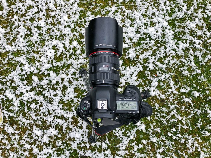 Una cámara réflex digital con lente de zoom descansando sobre la hierba nevada - equipo de fotografía de stock