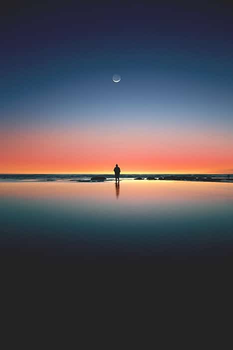 Impresionante retrato de una figura solitaria en una playa debajo de una colorida puesta de sol: simetría en la fotografía