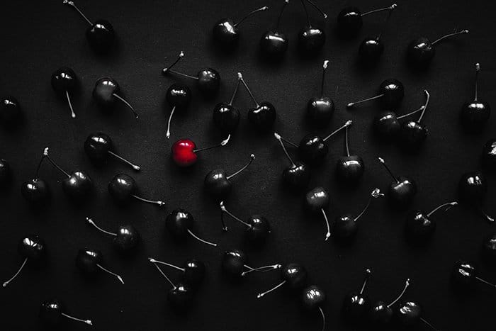 Elijah O'Donell fotografía aérea surrealista de cerezas negras, una roja, sobre una mesa negra