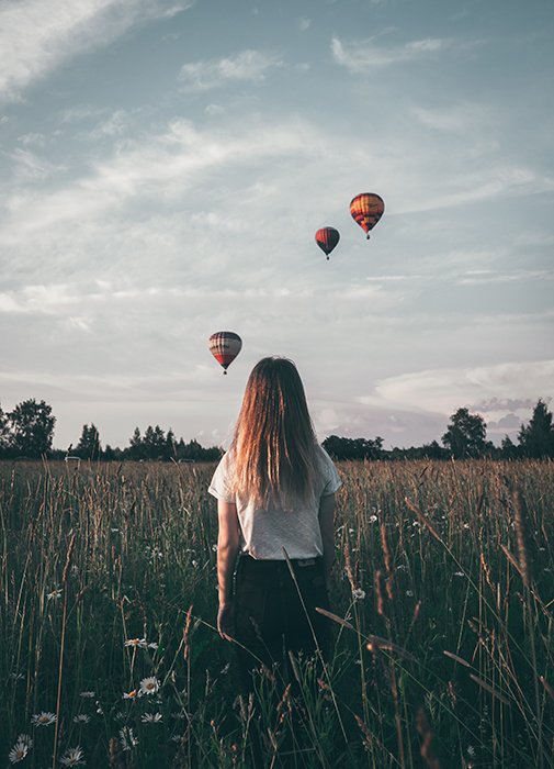 Natalya Letunova foto artística de una niña de pie en un campo mirando globos aerostáticos en el cielo - fotografía surrealista