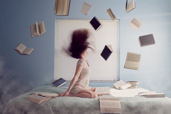 Fotografía surrealista de Laci Slezak de una niña sentada en una cama, libros volando alrededor.