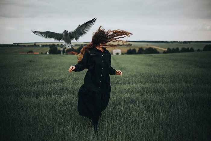 Foto de una mujer corriendo en un campo con un pájaro volando a su lado