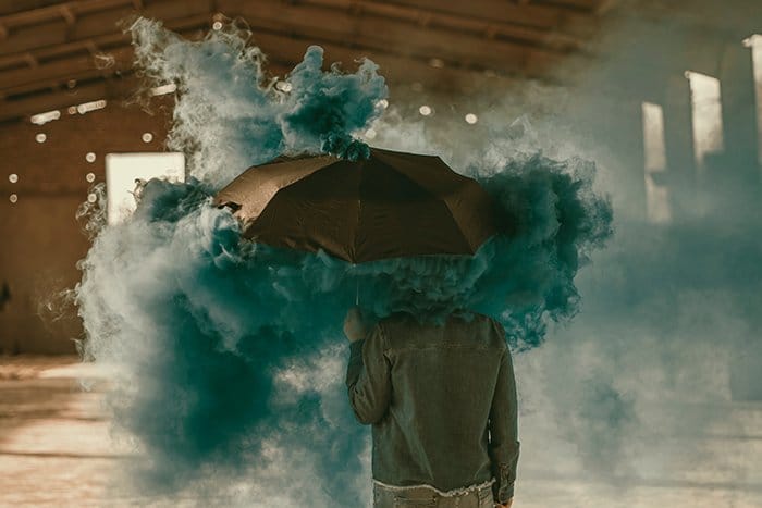 Foto surrealista de una persona de pie con un paraguas con el uso de una bomba de humo verde