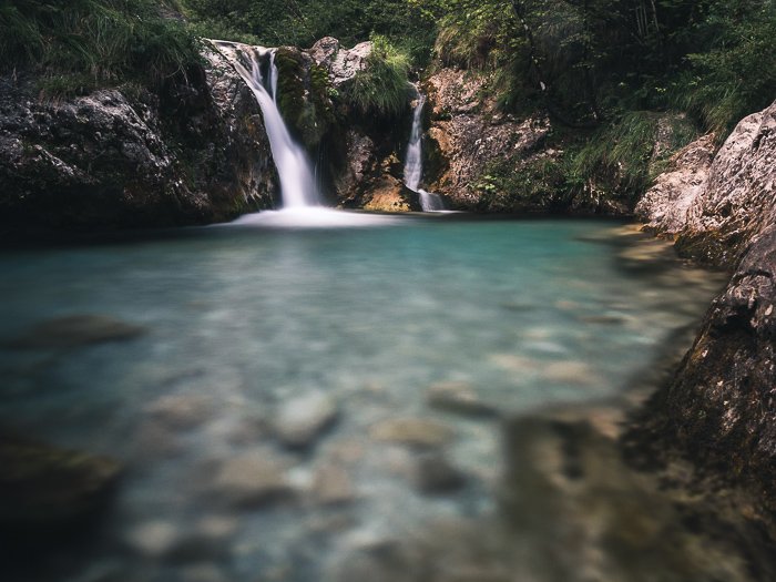 Una fotografía de verano de una cascada en Val Vertova