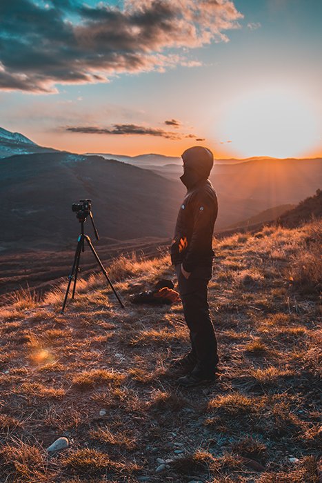 Un hombre en una montaña con un trípode y una cámara.