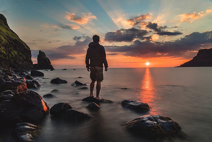 Un hombre mirando una puesta de sol en una playa rocosa