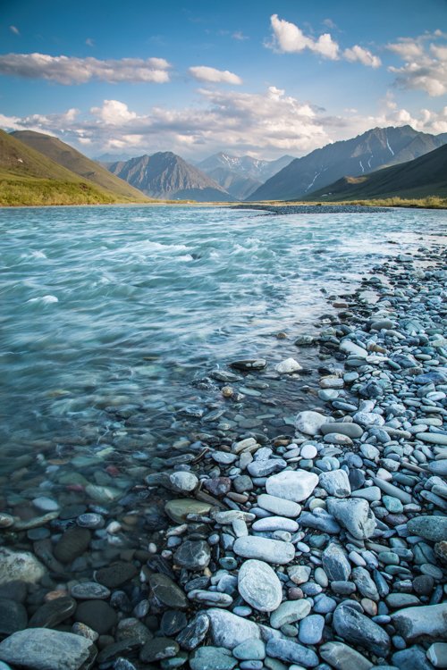 Un río con rocas en su orilla y montañas al fondo