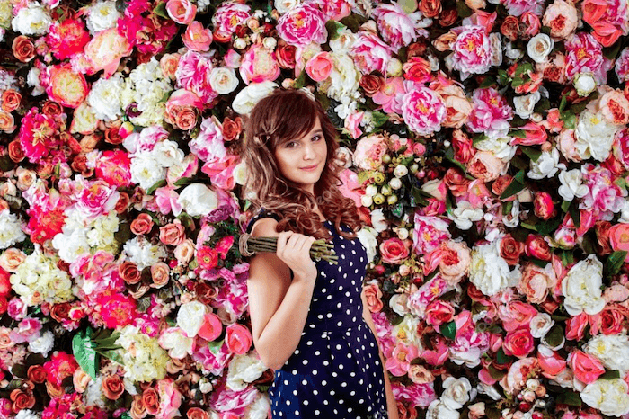 Una imagen de una mujer joven sosteniendo un ramo de pie contra un pozo de flores