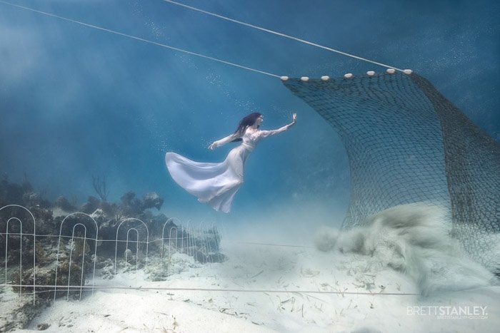 Retrato submarino de ensueño de un modelo femenino nadando hacia una red