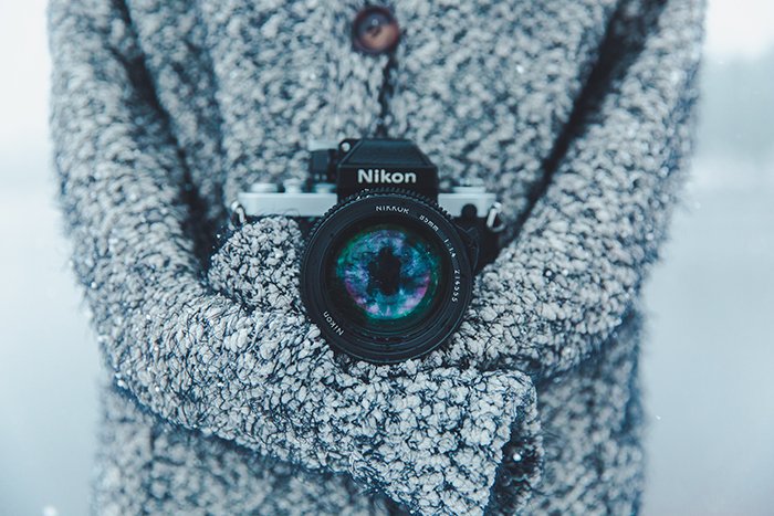 Un primer plano de una cámara Nikon alrededor del cuello de un fotógrafo, fotografiando retratos de nieve