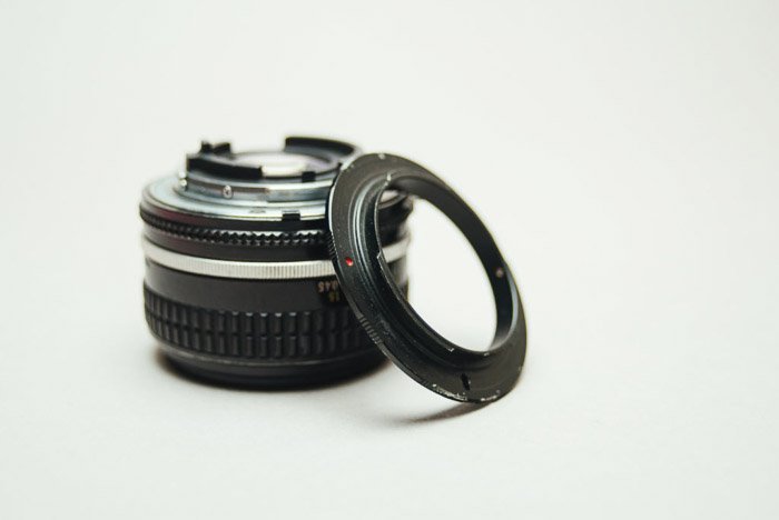 La lente de una cámara junto a un anillo de inversión sobre fondo blanco.