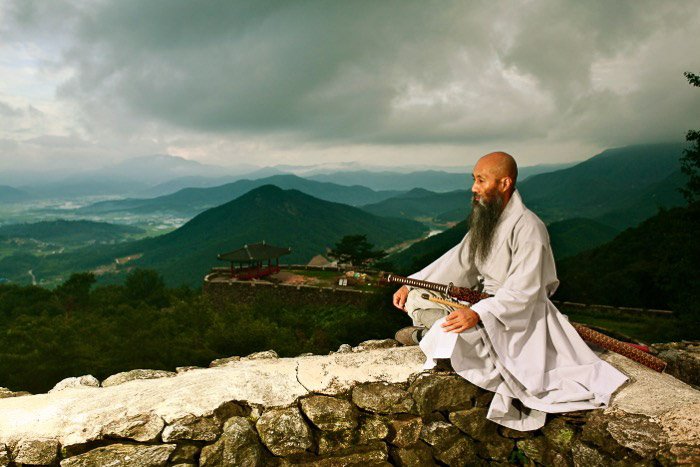 Un monje sentado en una pared mirando a lo lejos, con un hermoso paisaje montañoso detrás de él: la regla del espacio en la fotografía