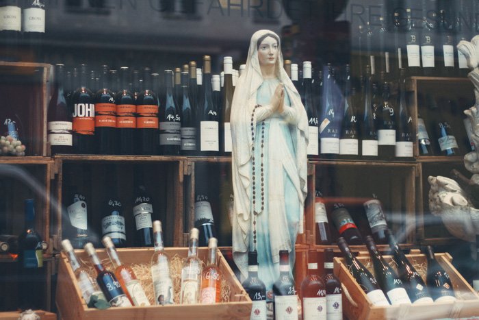 Una estatua de la Virgen María en el escaparate de una tienda de bebidas alcohólicas, tomada con una lente estándar