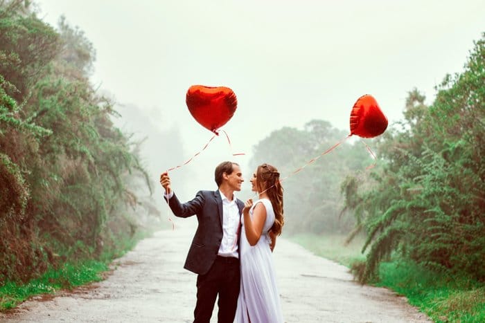 Una foto de una pareja elegante sosteniendo globos en forma de corazón.