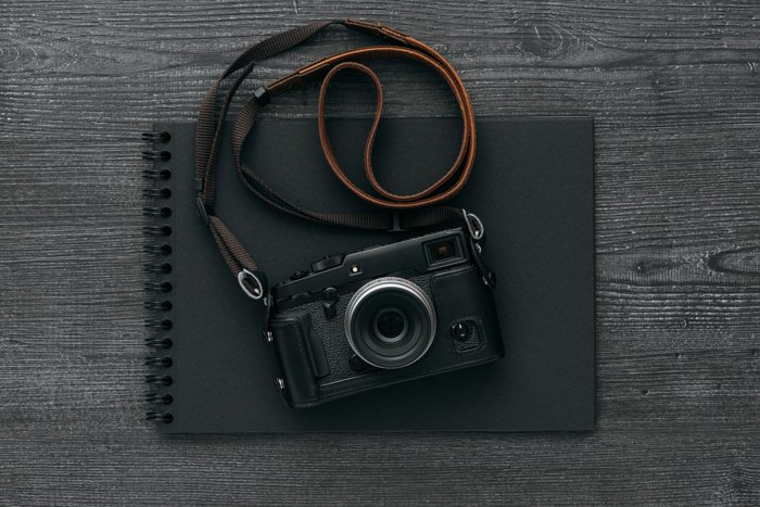 Álbum de fotos negro vacío y cámara digital profesional con una correa de cuero para cámara en un escritorio oscuro
