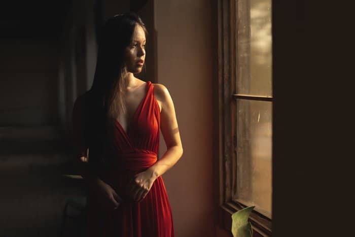 Foto de una mujer con un vestido rojo de pie junto a la ventana y mirando hacia afuera