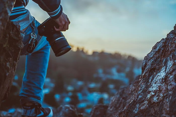 Primer plano de un fotógrafo de aventuras en solitario de pie sobre una roca y sosteniendo una cámara réflex digital