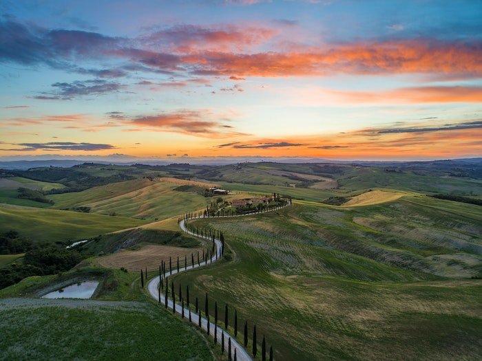 Imagen del paisaje de la puesta del sol de Toscana de un camino sinuoso y colinas verdes