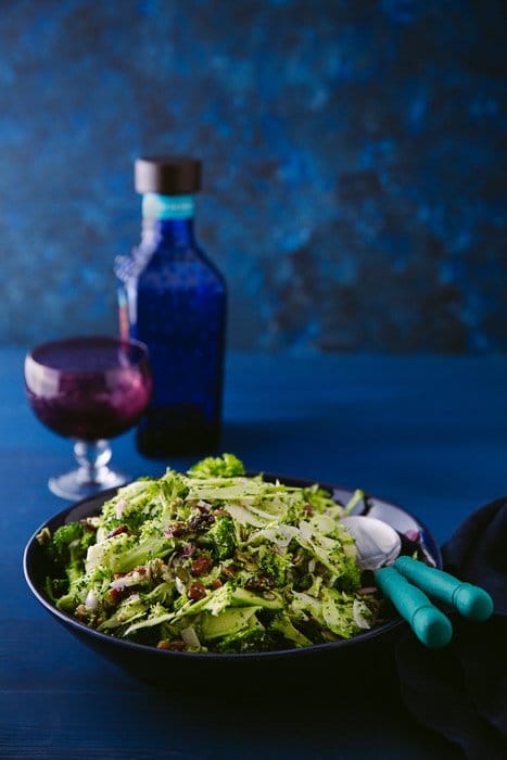 Hermosa fotografía de alimentos retrato de ensalada de brócoli, vinagre balsámico y un vaso contra un fondo azul.