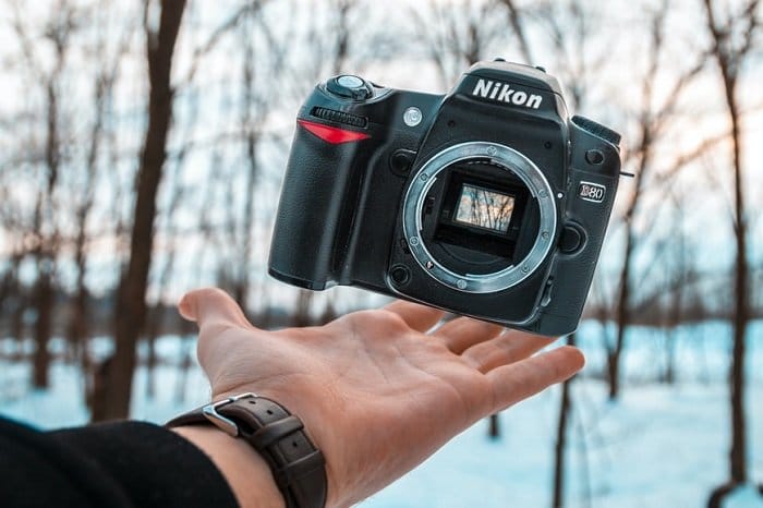 El fotógrafo lanza suavemente una cámara Nikon al aire debajo de su brazo extendido
