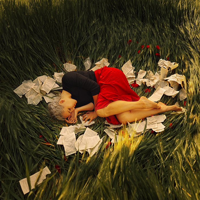 Un retrato de bellas artes de una modelo femenina acurrucada en la hierba rodeada de papel por Masha Sardari