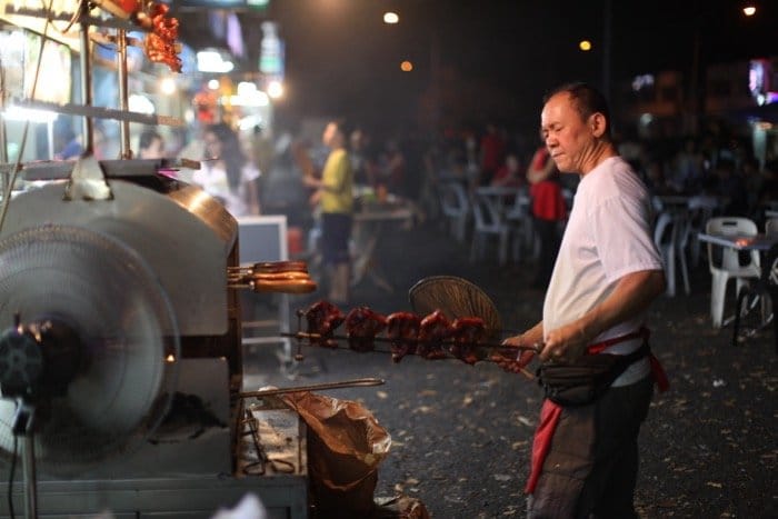 Fotografía con poca luz de un hombre cocinando carne en un mercado al aire libre.