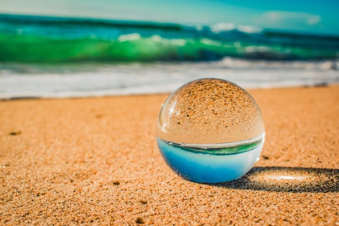 una bola de cristal tirada en la arena de una playa, la imagen reflejada en el interior