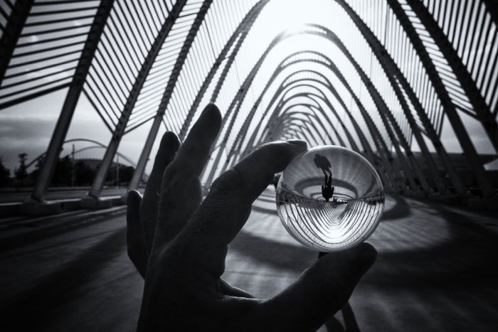 una mano sosteniendo una pequeña bola de lentes que refleja una foto de calle en blanco y negro 