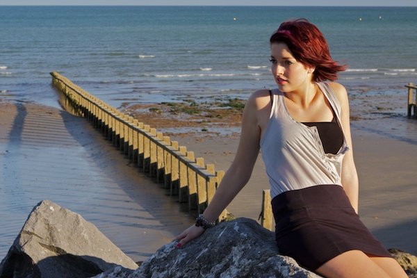 Foto de una mujer joven sentada sobre una roca en una playa mirando a la cámara