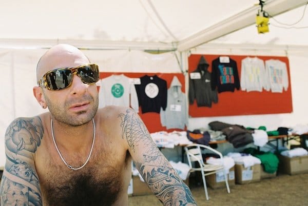 Foto de un hombre en topless con los brazos cubiertos de tatuajes y gafas de sol dentro de una tienda de merchandising