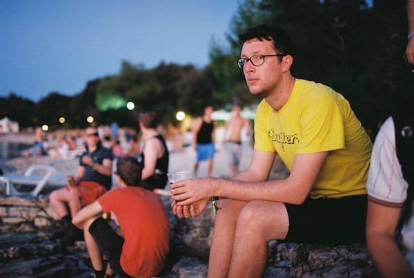 Foto de un joven con una camiseta amarilla en una especie de festival mirando a la cámara