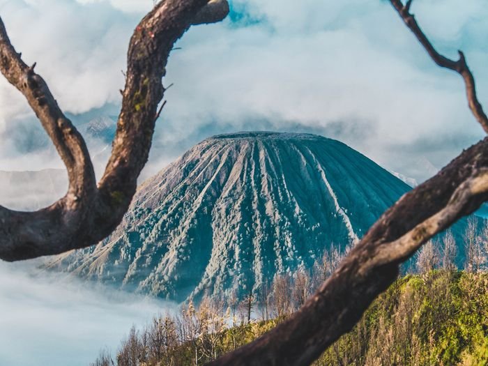 Foto de un volcán con ramas que enmarcan el primer plano