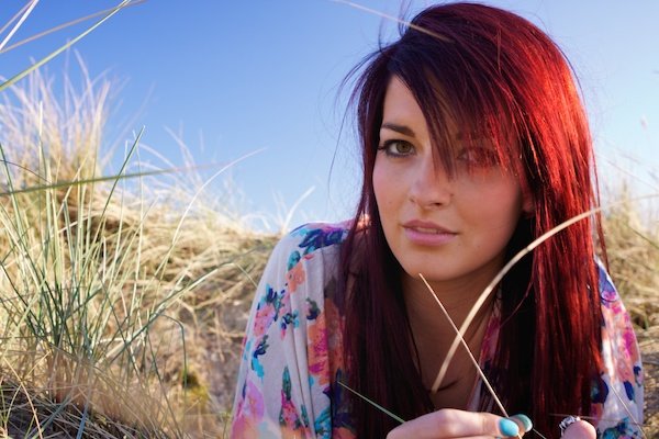 Chica de pelo rojo tendido en la hierba y sonriendo a la cámara