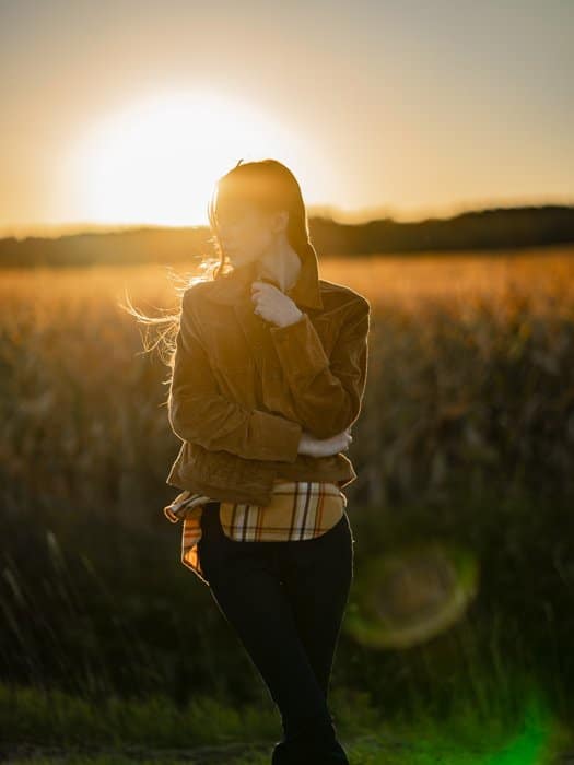 Una imagen de una mujer posando en un prado con el sol poniente detrás de ella