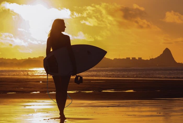 Una silueta de una mujer sosteniendo una tabla de surf en la playa con retroiluminación de sol poniente