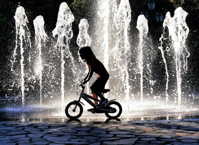 una imagen de un niño en bicicleta frente a una fuente retroiluminada