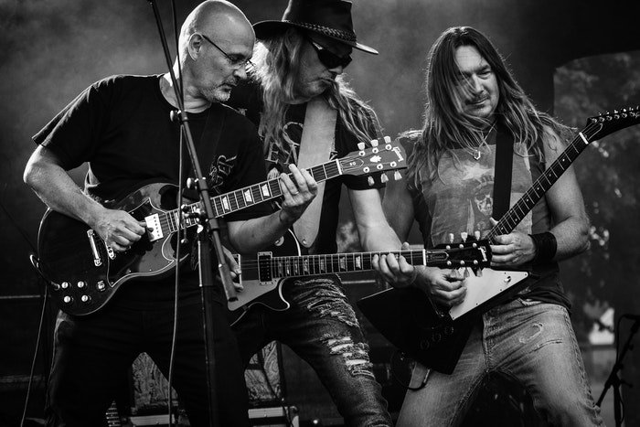 Un primer plano de tres guitarristas en el escenario durante un concierto en vivo