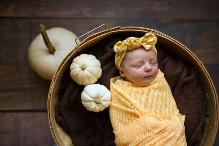 Foto de un bebé durmiendo con calabazas alrededor.
