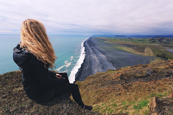 una mujer sentada en un acantilado con vistas a un hermoso paisaje costero: hermosos principios de fotografía